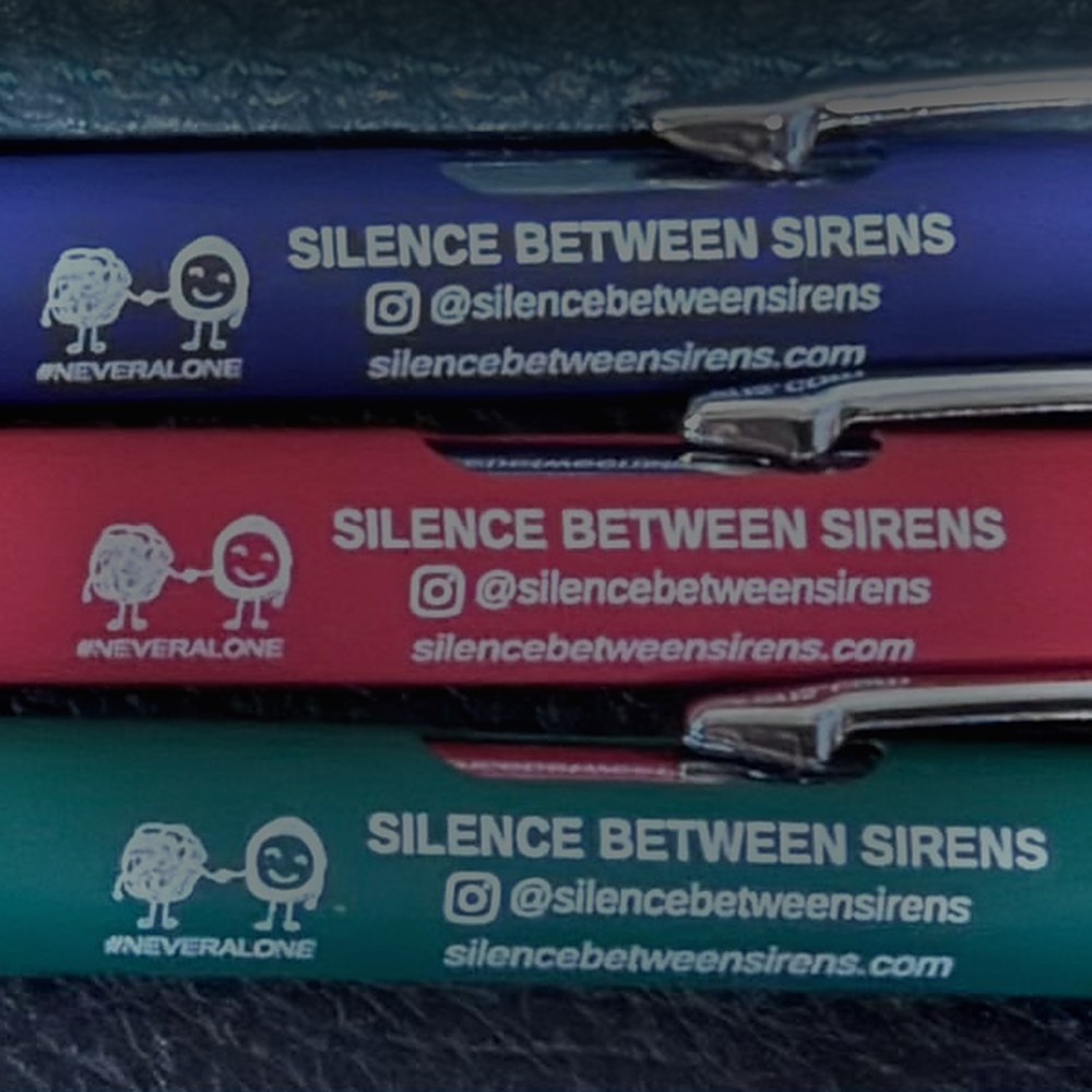 Three Silence Between Sirens soft touch metal pens in blue, red and green, printed with the #NeverAlone characters